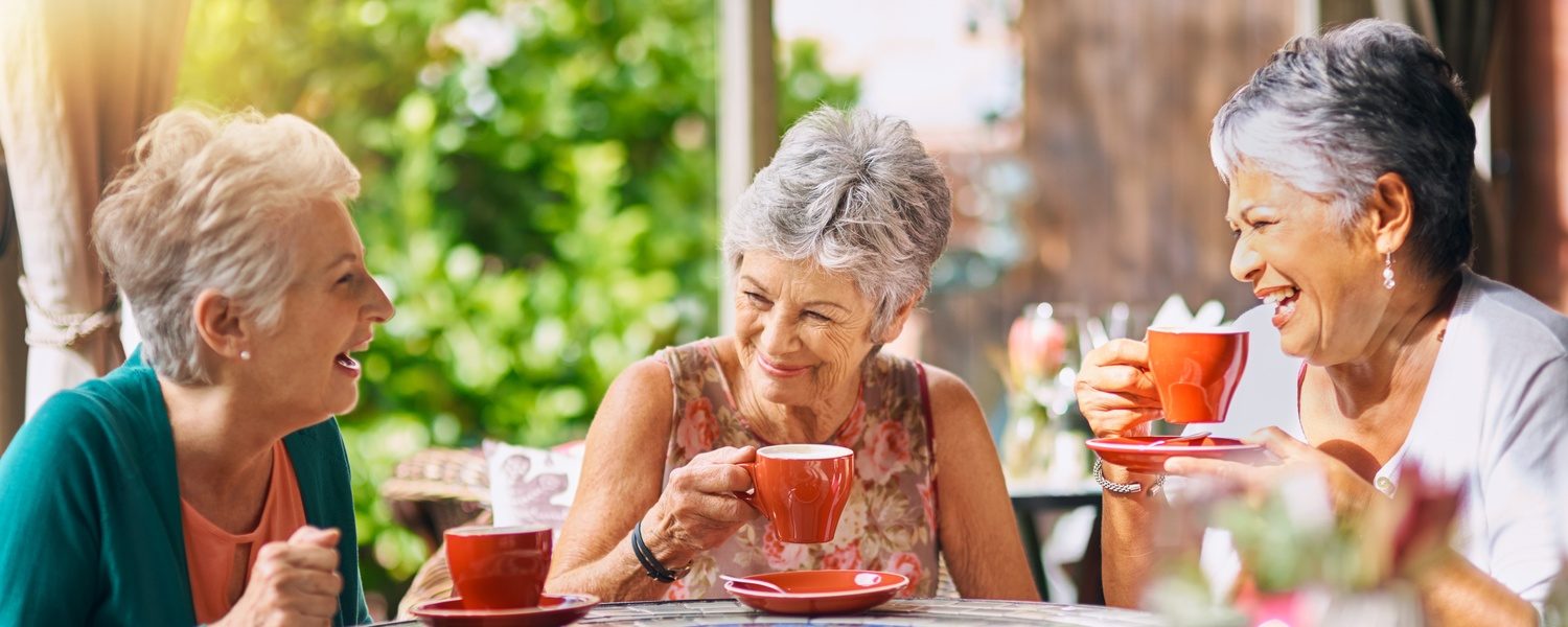 Two senior women talking and laughing together over coffee in a coffee shop